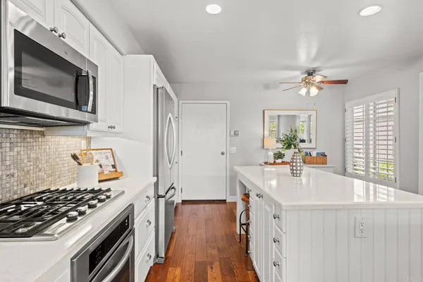 a kitchen with stainless steel appliances a stove a sink dishwasher a microwave oven with white cabinets and wooden floor