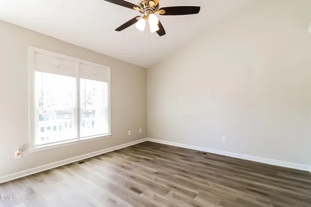 an empty room with wooden floor fan and windows