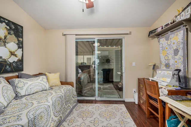 a bedroom with a bed a standing fan and a wooden floor
