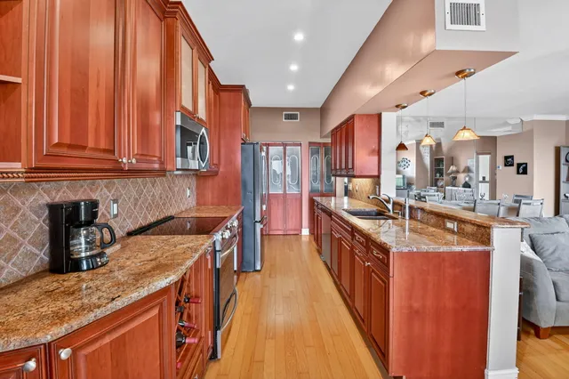 a large kitchen with stainless steel appliances granite countertop a stove a sink dishwasher and a refrigerator with wooden floor