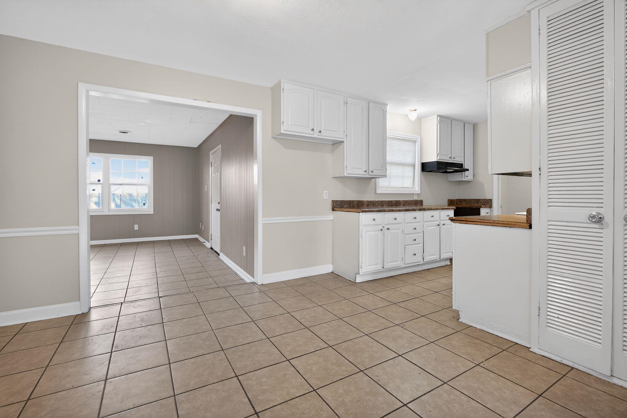 4828 Knight Arnold Road Memphis, TN 38118 - Photo 9 of 24 Kitchen with white cabinets, plenty of natural light, dark countertops, light tile patterned floors, and wooden walls