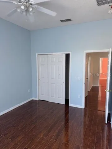 a view of an empty room with wooden floor and a ceiling fan