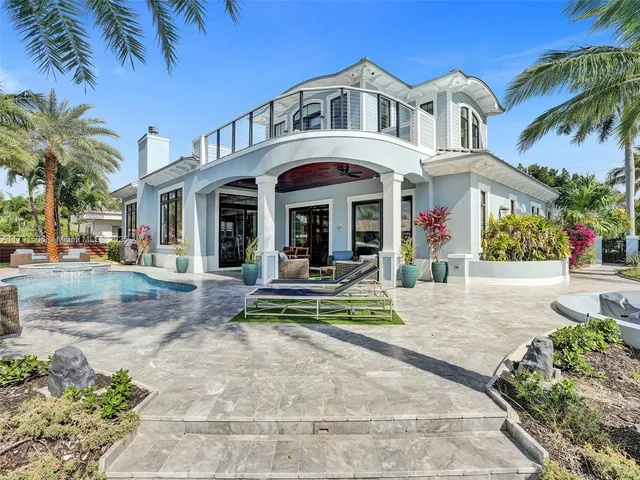 a view of a white house with a large swimming pool and a lawn chairs under palm trees