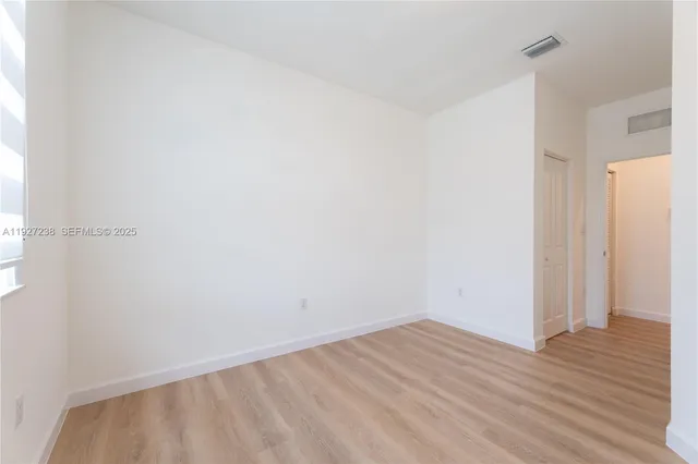 a view of an empty room with wooden floor and a bathroom