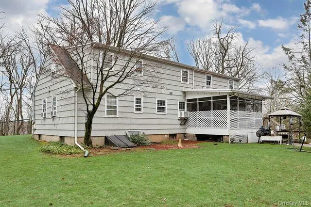 a view of a white house in front of a big yard with plants and large trees