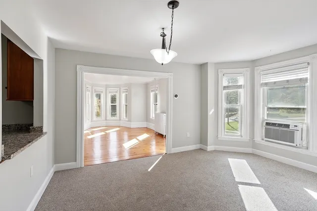 a view of an empty room with window and kitchen view