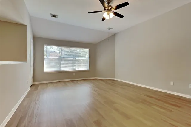 an empty room with wooden floor fan and windows