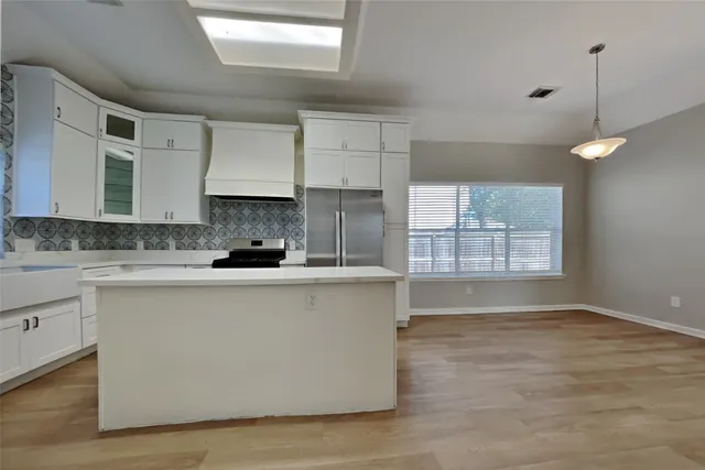 a large kitchen with granite countertop a stove a sink a refrigerator and white cabinets with wooden floor