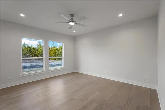 an empty room with wooden floor fan and windows