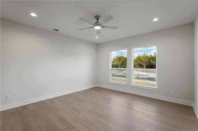 an empty room with wooden floor fan and windows