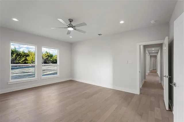 an empty room with wooden floor a ceiling fan and windows