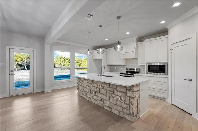 a kitchen with stainless steel appliances granite countertop a stove top oven a sink dishwasher and a refrigerator with wooden floor