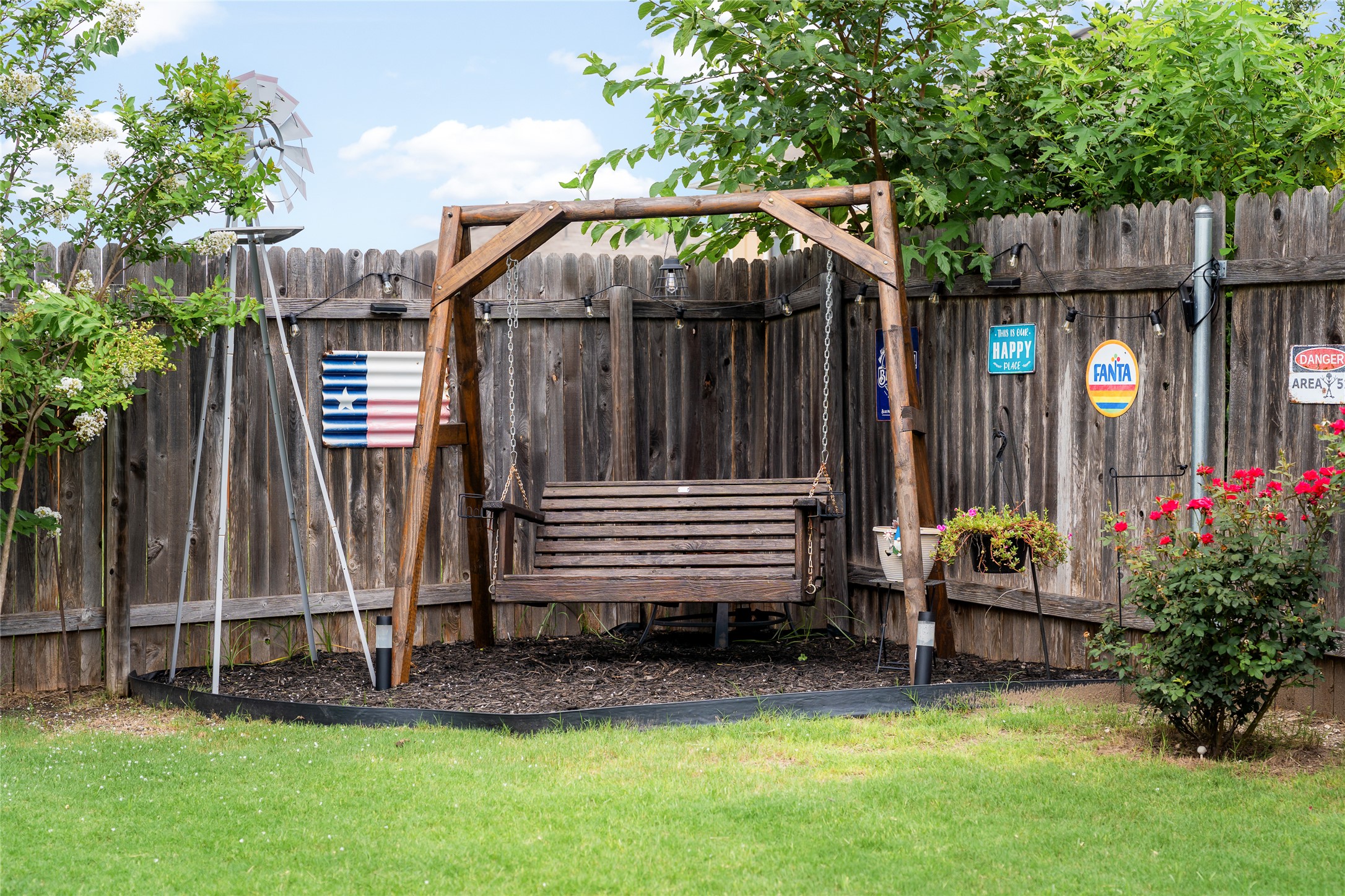 249 Wapiti Road Buda, TX 78610 - Photo 20 of 21 A tranquil outdoor space offers a wooden swing set against a rustic fence, framed by lush greenery.