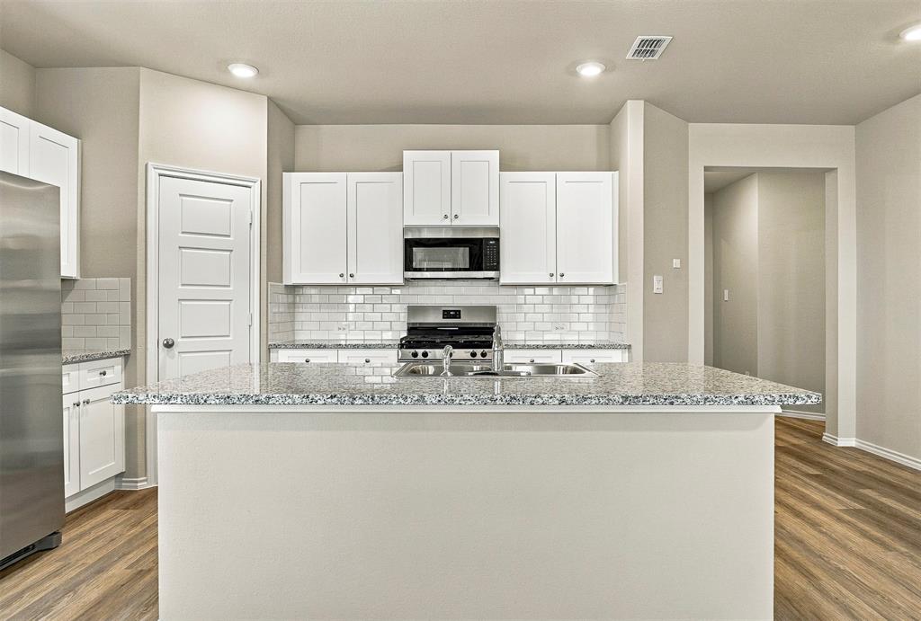 15932 Stableford Road Justin, TX 76247 - Photo 9 of 35 Kitchen featuring white cabinetry, subway tile backsplash, stainless steel appliances, wood-finish flooring, and a breakfast bar with stone countertops