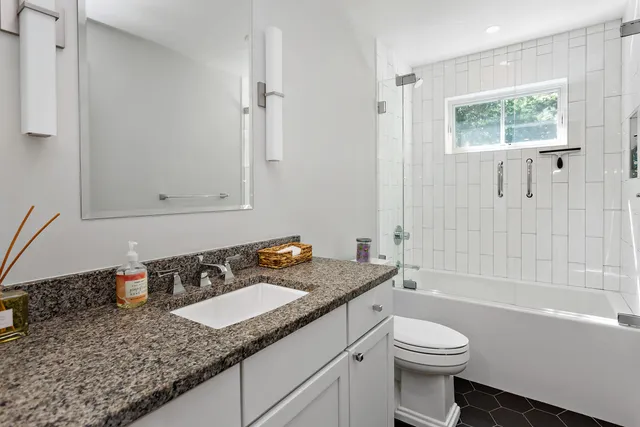 a bathroom with a granite countertop sink a toilet a mirror and shower