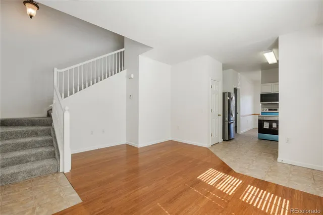 a view of an empty room with wooden floor and a kitchen