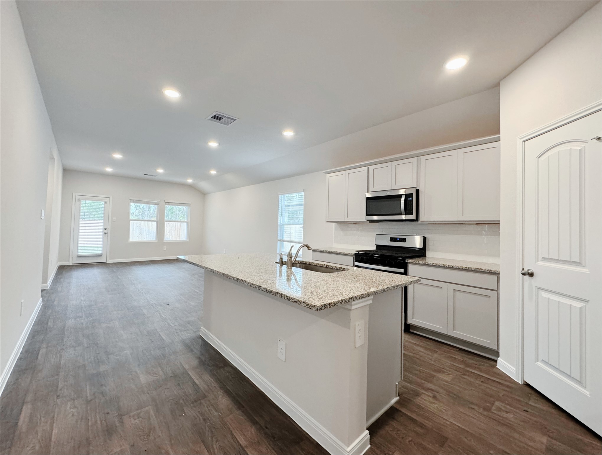 204 Addison Place Lockhart, TX 78644 - Photo 3 of 39 Kitchen with stainless steel appliances, a kitchen island with sink, light stone counters, recessed lighting, and dark wood-style flooring