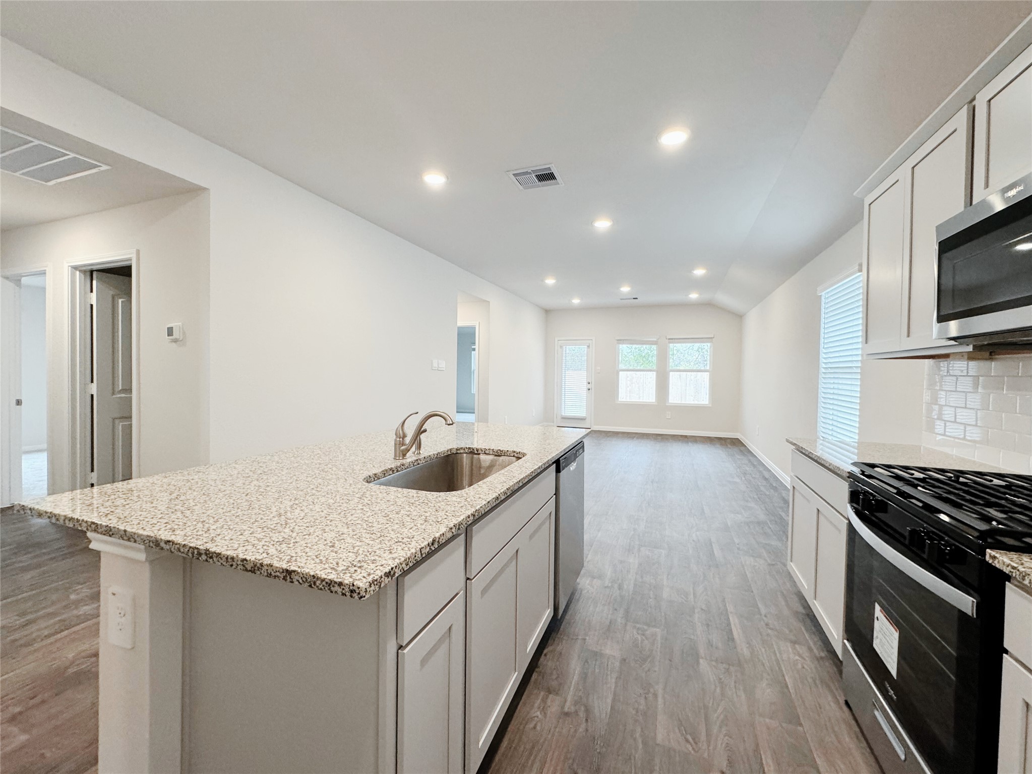 204 Addison Place Lockhart, TX 78644 - Photo 5 of 39 Kitchen with dark wood-style floors, light stone countertops, lofted ceiling, a center island with sink, and recessed lighting
