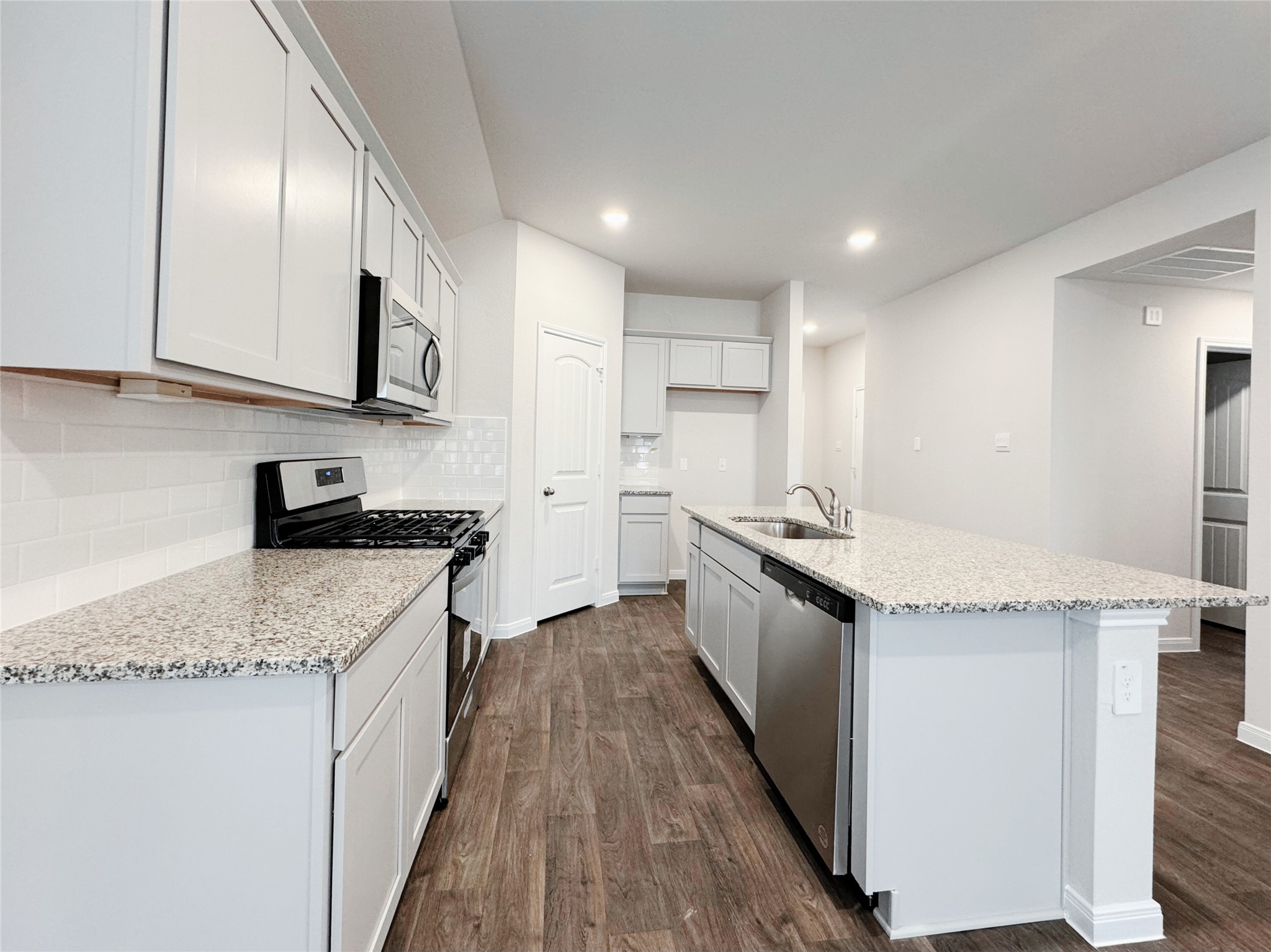 204 Addison Place Lockhart, TX 78644 - Photo 6 of 39 Kitchen featuring stainless steel appliances, dark wood-style flooring, light stone counters, a center island with sink, and backsplash