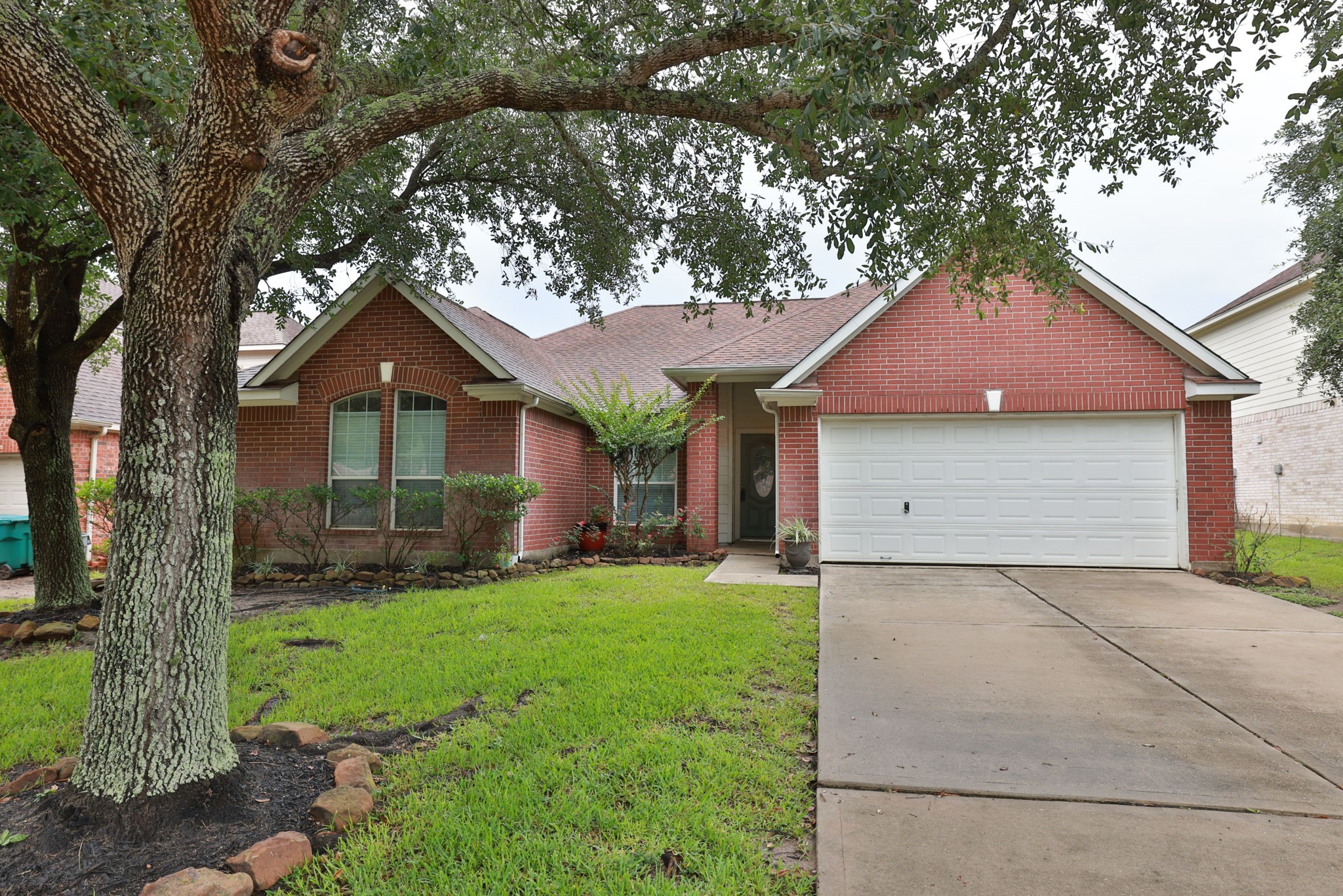 This charming home features a classic brick exterior, a two-car garage, and a well-maintained front lawn. A mature tree offers shade, providing a welcoming and serene atmosphere.