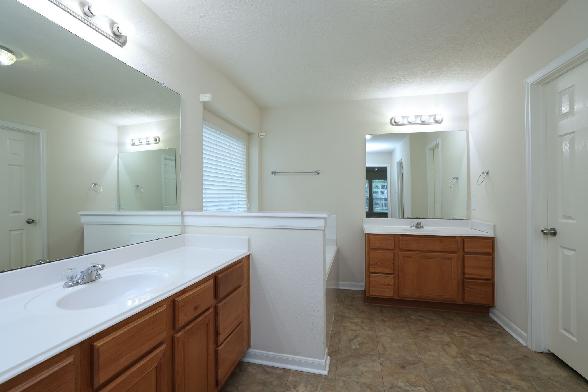 30515 Red Bluff Circle Magnolia, TX 77355 - Photo 17 of 28 This primary bathroom features dual sinks with spacious countertops and wooden cabinets, large mirrors, and bright lighting. The neutral tile floor complements the clean, modern design, and there's ample natural light from the window.