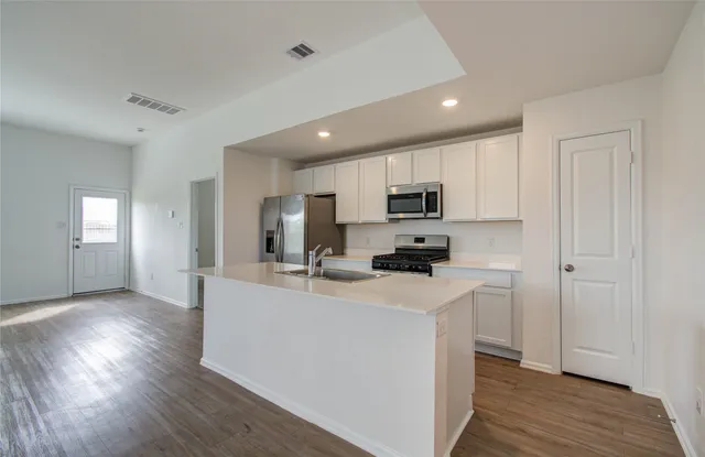 a kitchen with stainless steel appliances a sink a stove a refrigerator cabinets and wooden floor