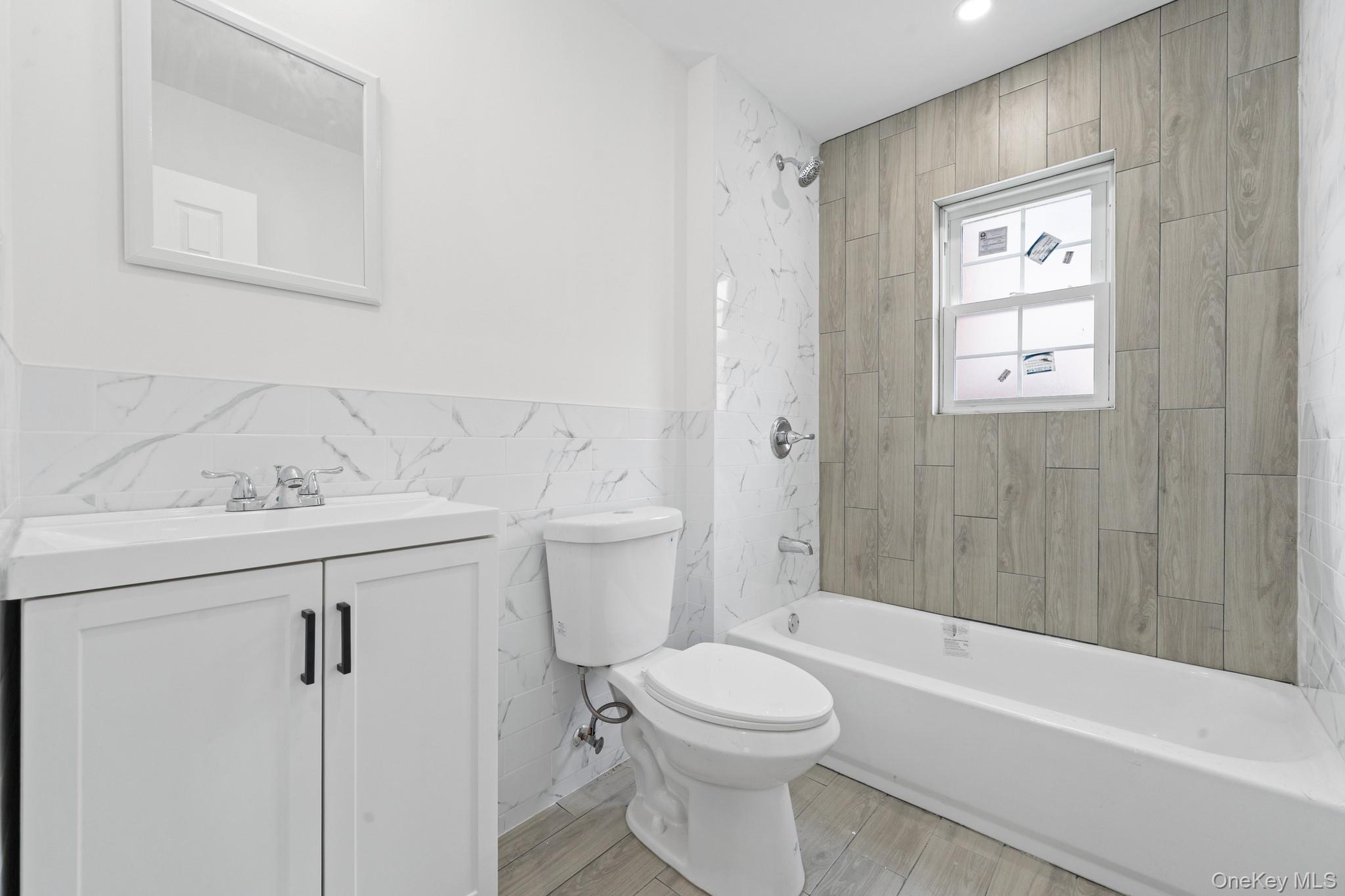 223-12 134th Road Queens, NY 11413 - Photo 10 of 17 Full bath with tile walls, tub / shower combination, vanity, a wainscoted wall, and light wood finished floors