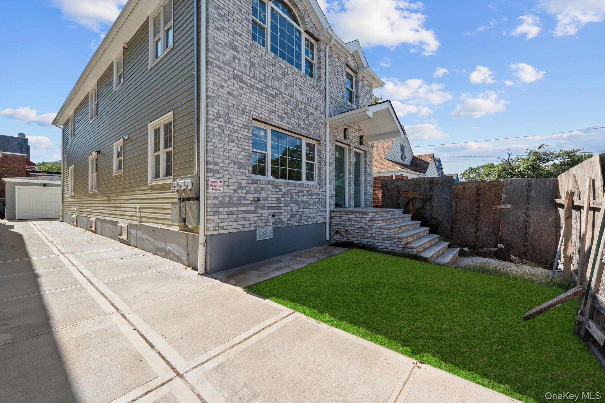 223-12 134th Road Queens, NY 11413 - Photo 14 of 17 View of side of property with brick siding, a garage, and concrete driveway