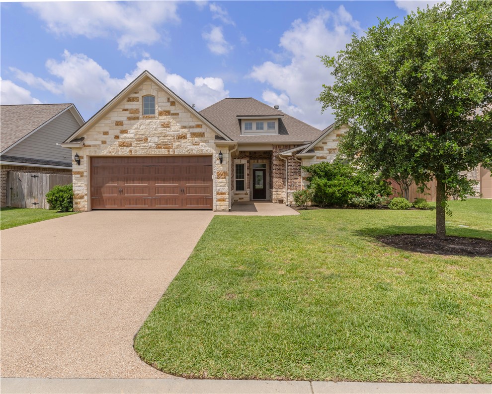 View of front of home with stone siding, driveway, an attached garage, and a shingled roof