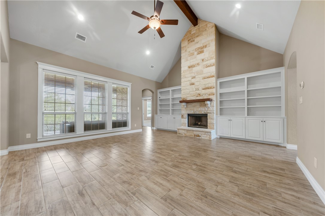 3520 Foxcroft Path Bryan, TX 77808 - Photo 4 of 28 Unfurnished living room featuring arched walkways, beam ceiling, high vaulted ceiling, a stone fireplace, and light wood-type flooring