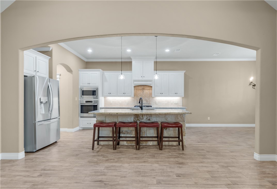 3520 Foxcroft Path Bryan, TX 77808 - Photo 7 of 28 Kitchen featuring arched walkways, stainless steel appliances, a kitchen breakfast bar, pendant lighting, and backsplash