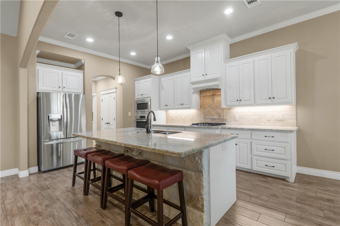 3520 Foxcroft Path Bryan, TX 77808 - Photo 8 of 28 Kitchen featuring arched walkways, appliances with stainless steel finishes, a breakfast bar area, light stone counters, and a center island with sink