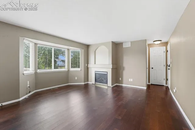 an empty room with wooden floor fireplace and windows