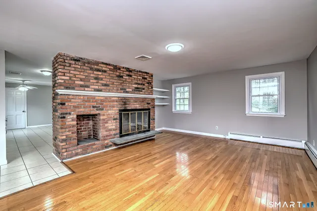 a view of an empty room with wooden floor fireplace and a window