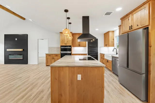 a kitchen with stainless steel appliances granite countertop a refrigerator a sink dishwasher a oven and a dining table with wooden floor