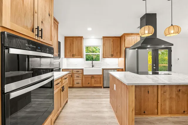 a kitchen with stainless steel appliances granite countertop a refrigerator a sink dishwasher a oven and a dining table with wooden floor