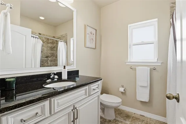 a bathroom with a granite countertop toilet a sink a mirror and a window