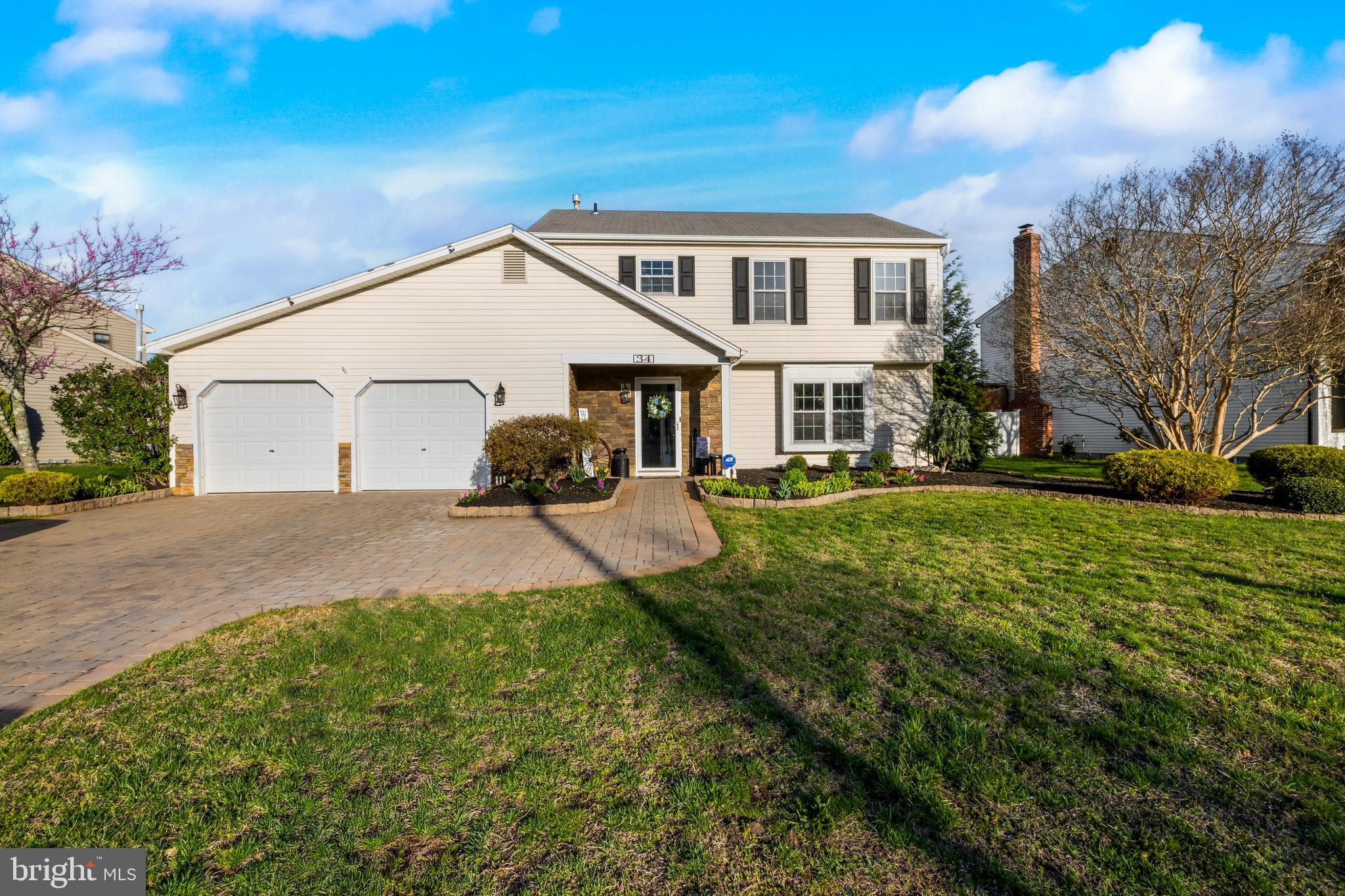 a view of a white house in front of a big yard with plants and large trees