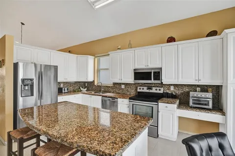 a kitchen with stainless steel appliances granite countertop a stove top oven a sink a refrigerator white cabinets and a refrigerator