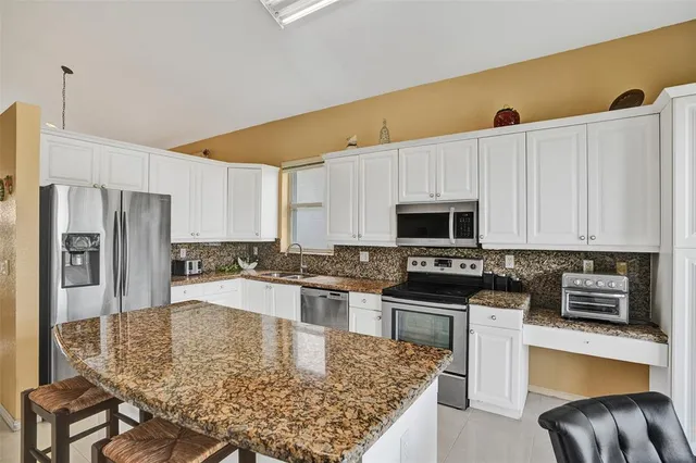 a kitchen with stainless steel appliances granite countertop a stove top oven a sink a refrigerator white cabinets and a refrigerator