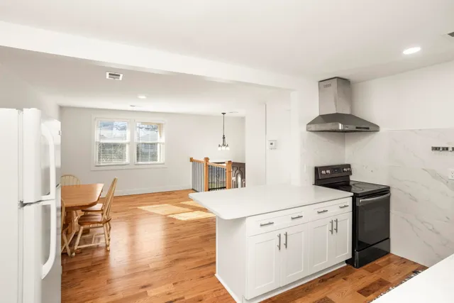 a kitchen with stainless steel appliances granite countertop a stove a sink dishwasher and white cabinets with wooden floor