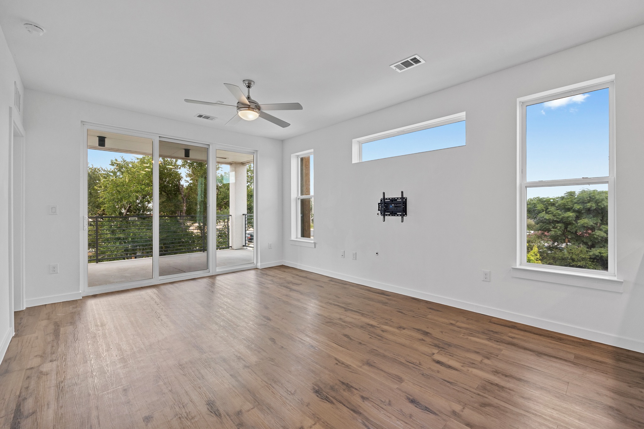 4801 Springdale Road, Unit 2301 Austin, TX 78723 - Photo 7 of 36 A spacious room features a sleek ceiling fan and natural wood flooring, opening to a private balcony.