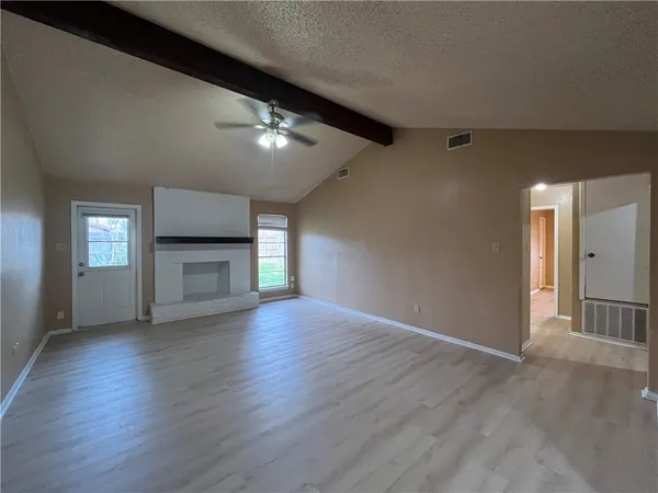 an empty room with wooden floor fireplace and windows