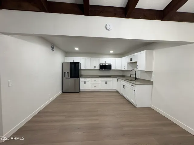 a large kitchen with stainless steel appliances kitchen island a sink dishwasher a refrigerator and white cabinets with wooden floor