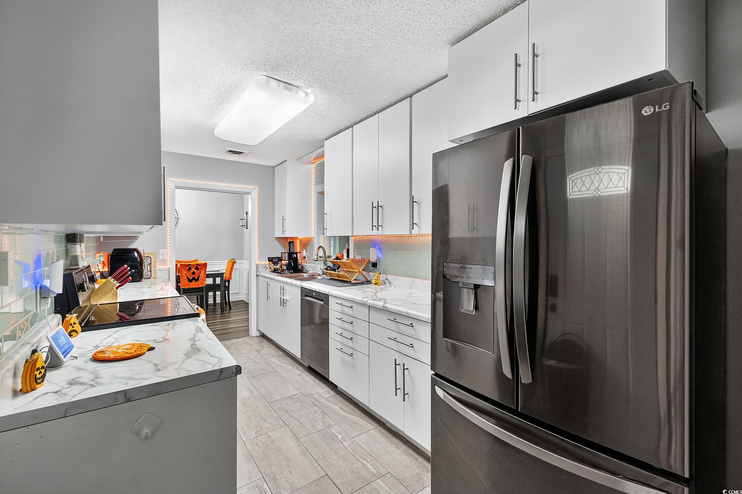 342 Red Fox Road Myrtle Beach, SC 29579 - Photo 11 of 40 Kitchen with stainless steel appliances, decorative backsplash, a textured ceiling, white cabinetry, and light stone countertops