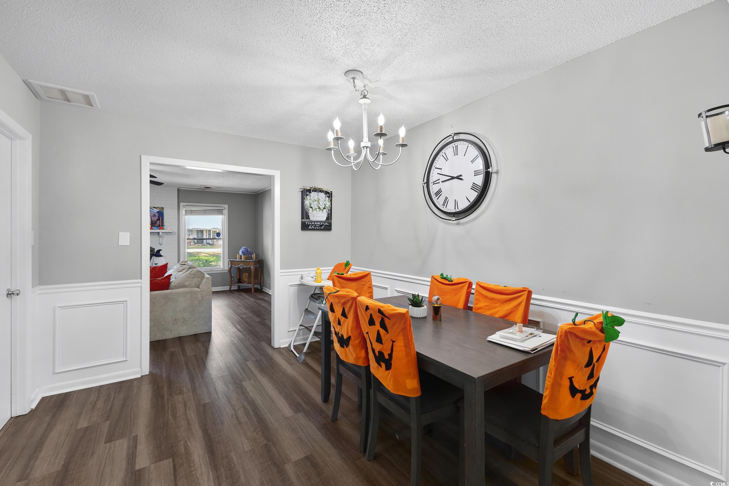 342 Red Fox Road Myrtle Beach, SC 29579 - Photo 16 of 40 Dining area featuring a wainscoted wall, a decorative wall, dark wood-type flooring, a textured ceiling, and a chandelier