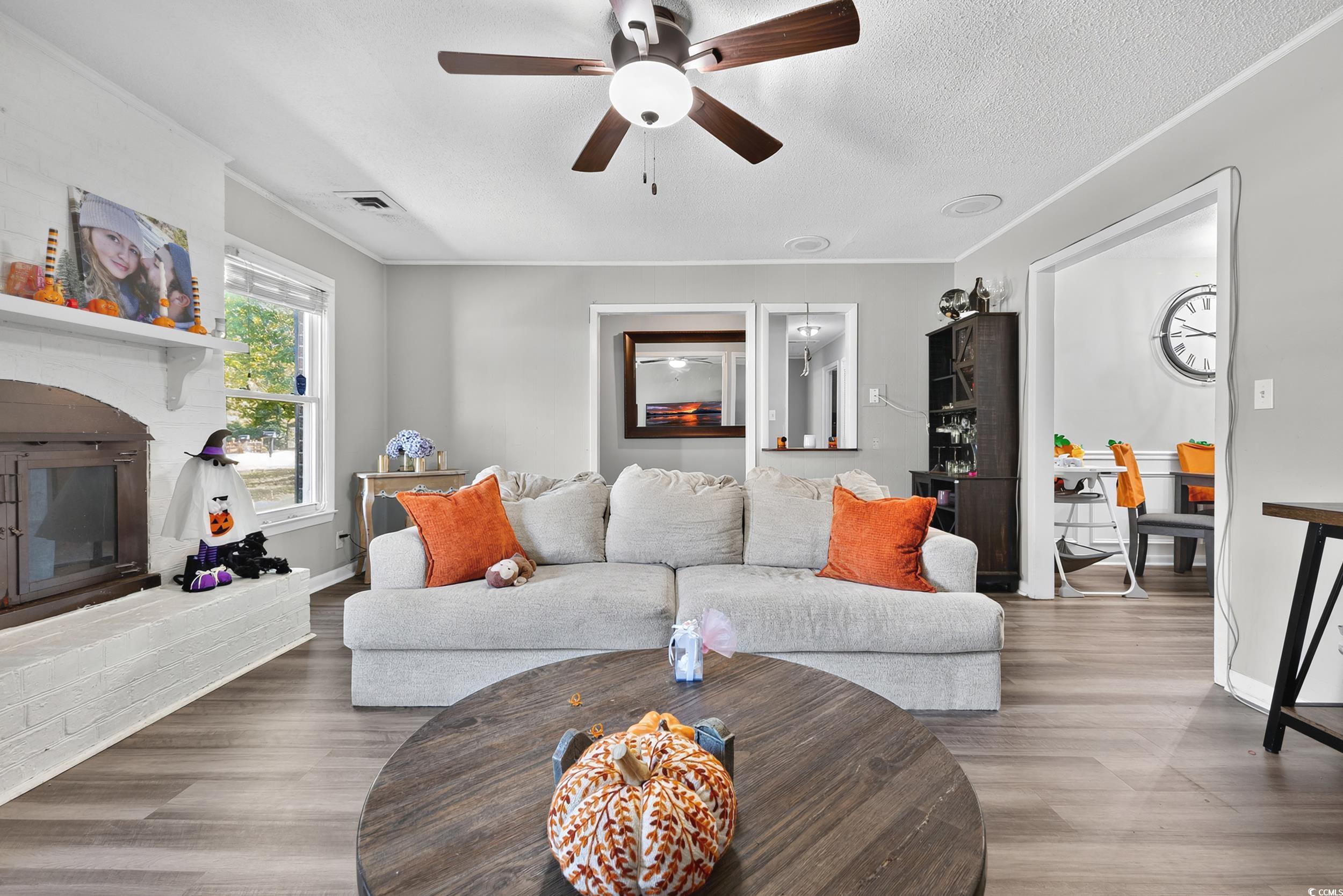 342 Red Fox Road Myrtle Beach, SC 29579 - Photo 6 of 40 Living room featuring ceiling fan, a brick fireplace, wood finished floors, a textured ceiling, and ornamental molding