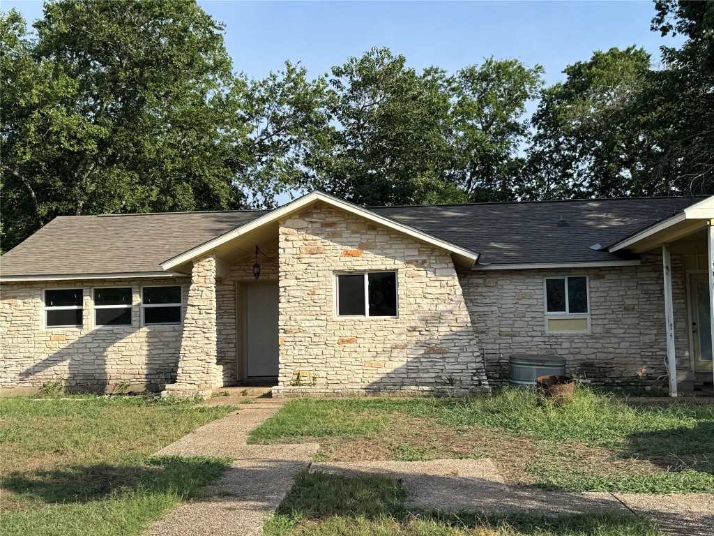 Ranch-style home with stone siding, a shingled roof, and a front yard