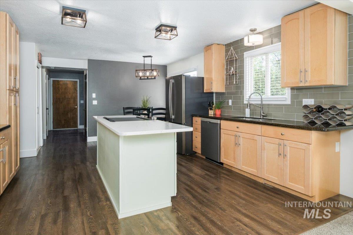 1401 Chokecherry Drive Pocatello, ID 83204 - Photo 14 of 46 Kitchen featuring a central island with a white countertop, wood-finish flooring, light wood cabinetry, a dark countertop, and a gray subway tile backsplash