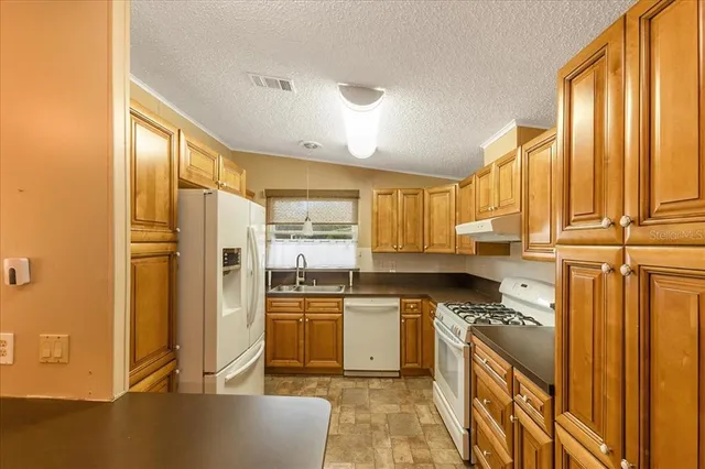 a kitchen with granite countertop a refrigerator a sink and white cabinets